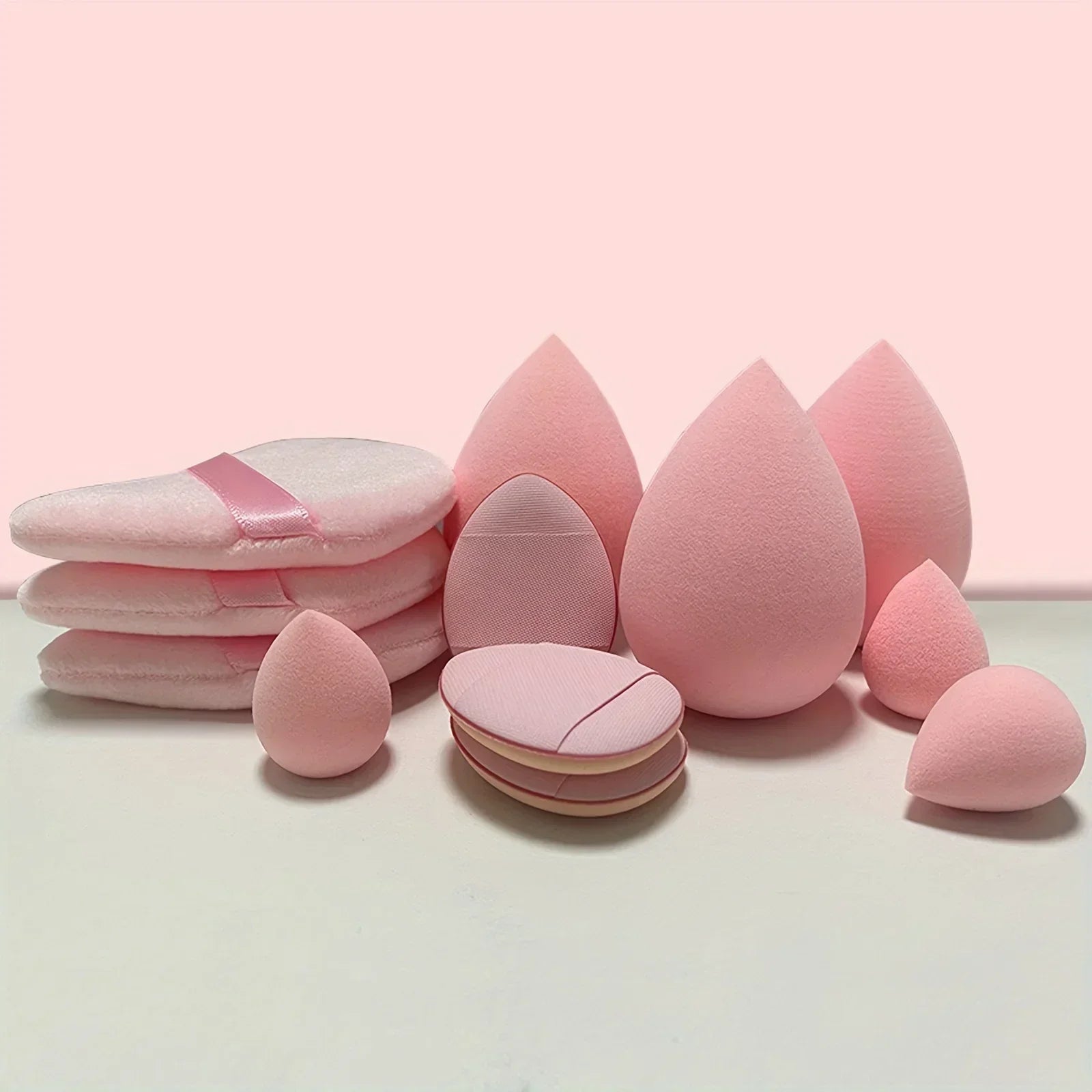 Pink makeup sponges and foundation puffs on white surface, beauty tools set.