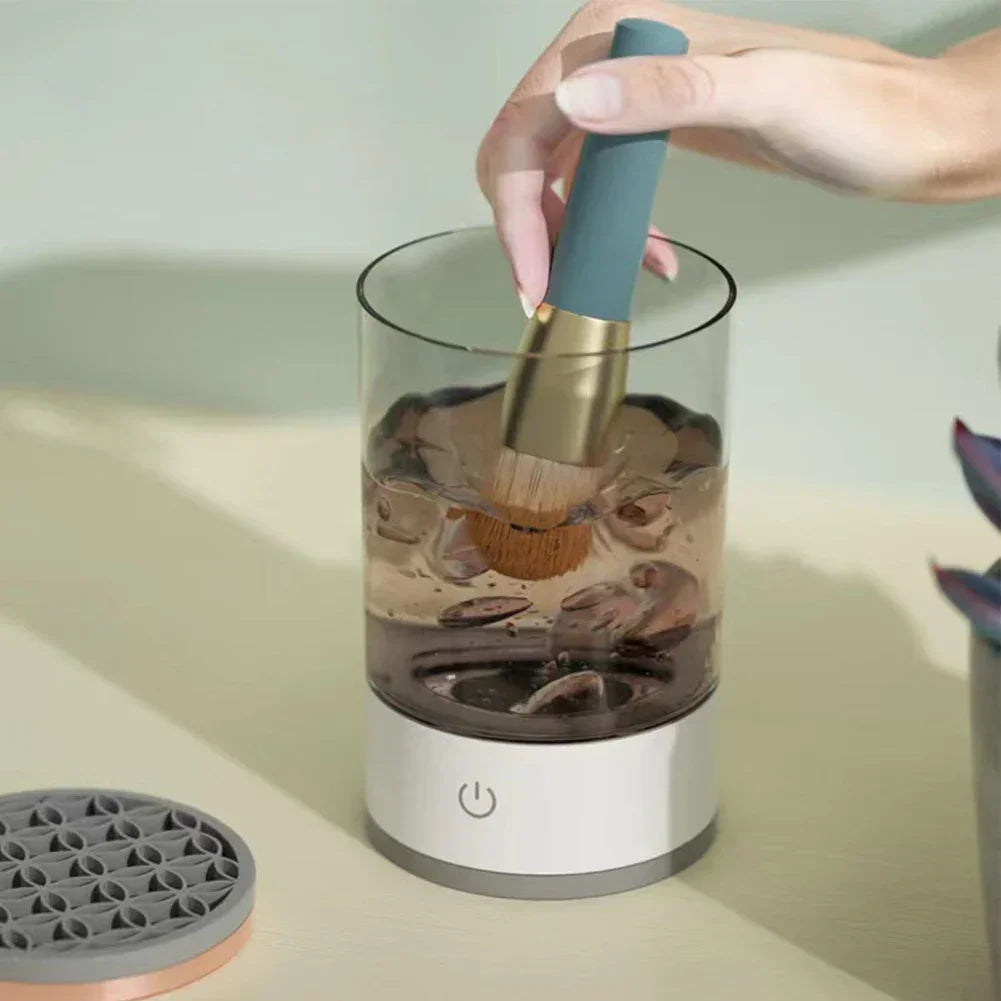 Electric makeup brush cleaner in use with water, modern design on beige surface
