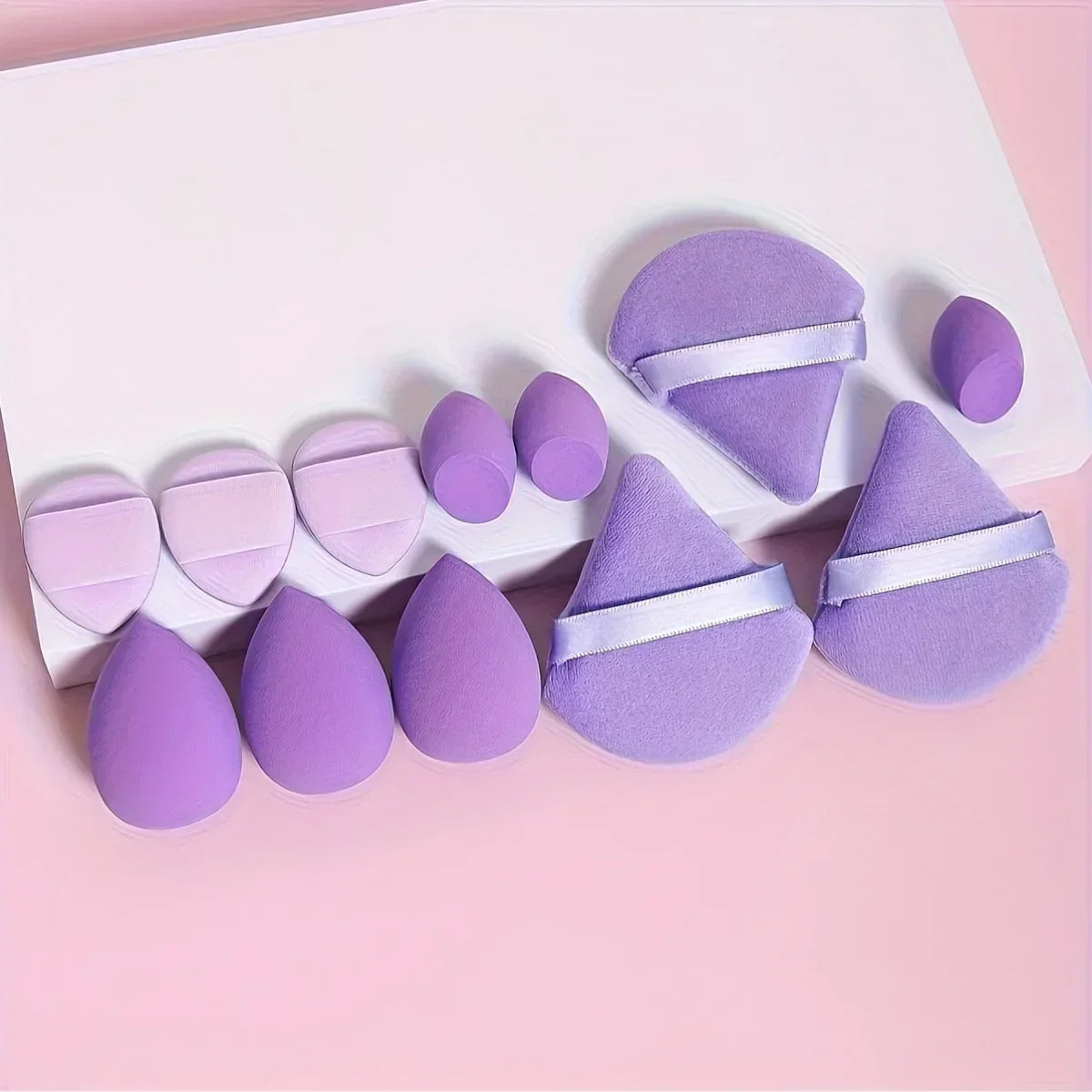 Set of purple makeup sponges and powder puffs arranged on a pink background