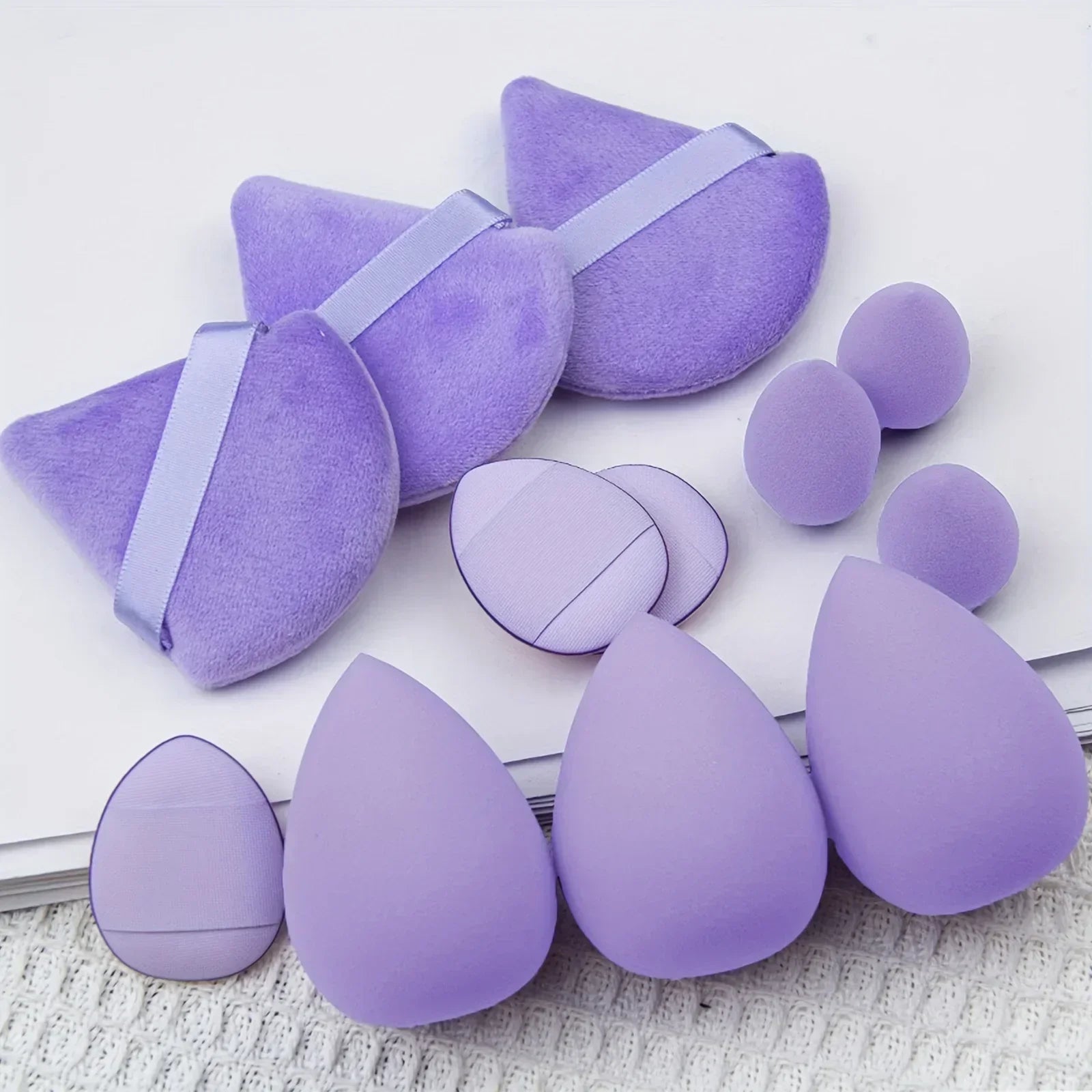 Set of purple makeup sponges and powder puffs on a white surface